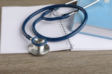 Book, stethoscope and notebook on wooden table, closeup. Medical education