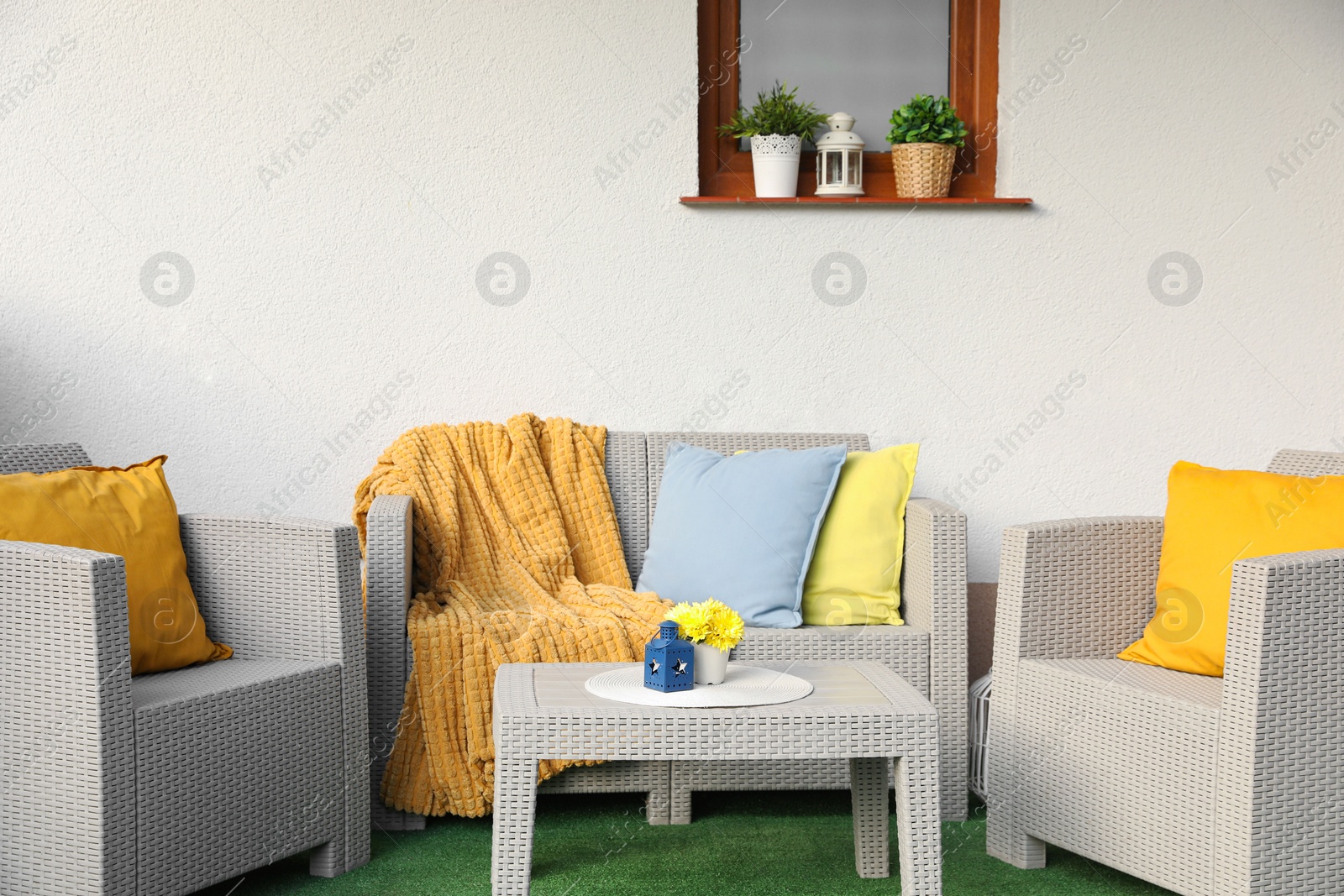 Photo of Beautiful rattan garden furniture, soft pillows, blanket and yellow chrysanthemum flowers near white wall