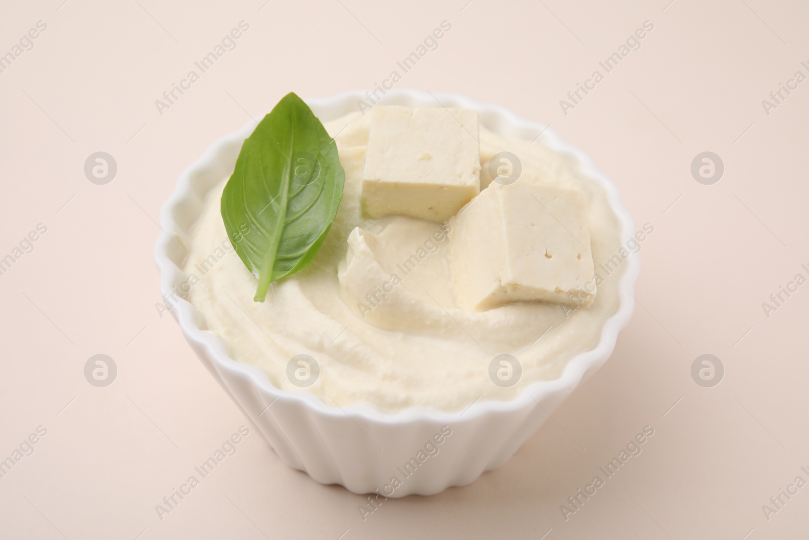 Photo of Delicious tofu sauce and basil leaf in bowl on beige background, closeup