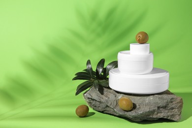 Jars of natural cream, stone and olives on light green background, space for text. Cosmetic products