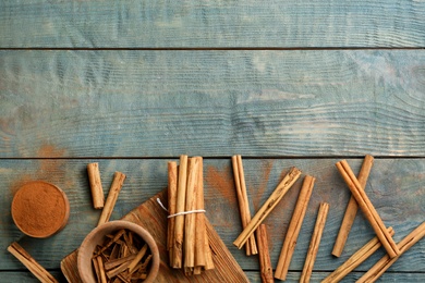 Photo of Aromatic cinnamon sticks and powder on light blue wooden table, flat lay. Space for text
