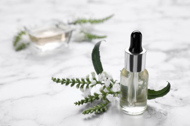 Bottle of essential oil and flowers on white marble table, closeup. Space for text