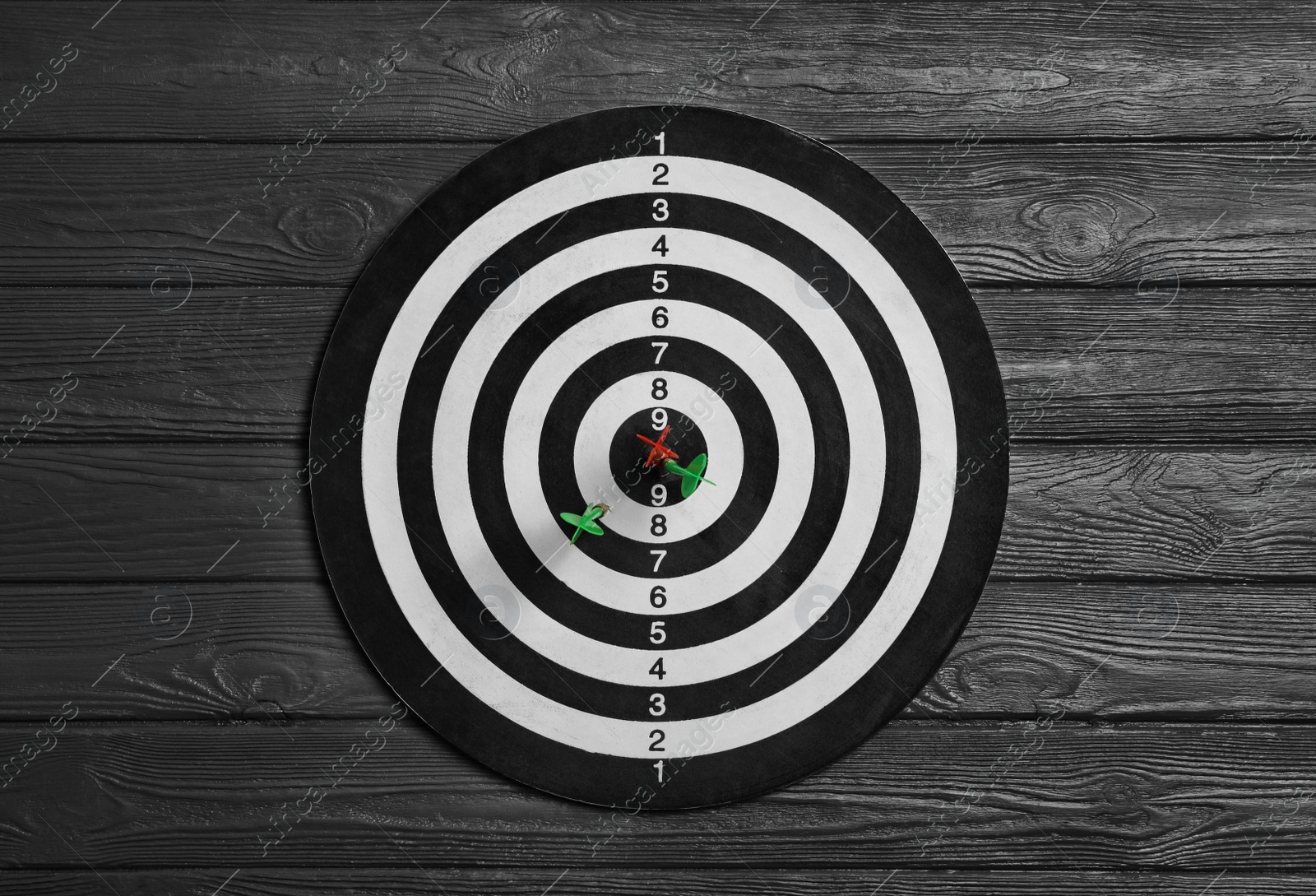 Photo of Dart board with color arrows on black wooden background, top view