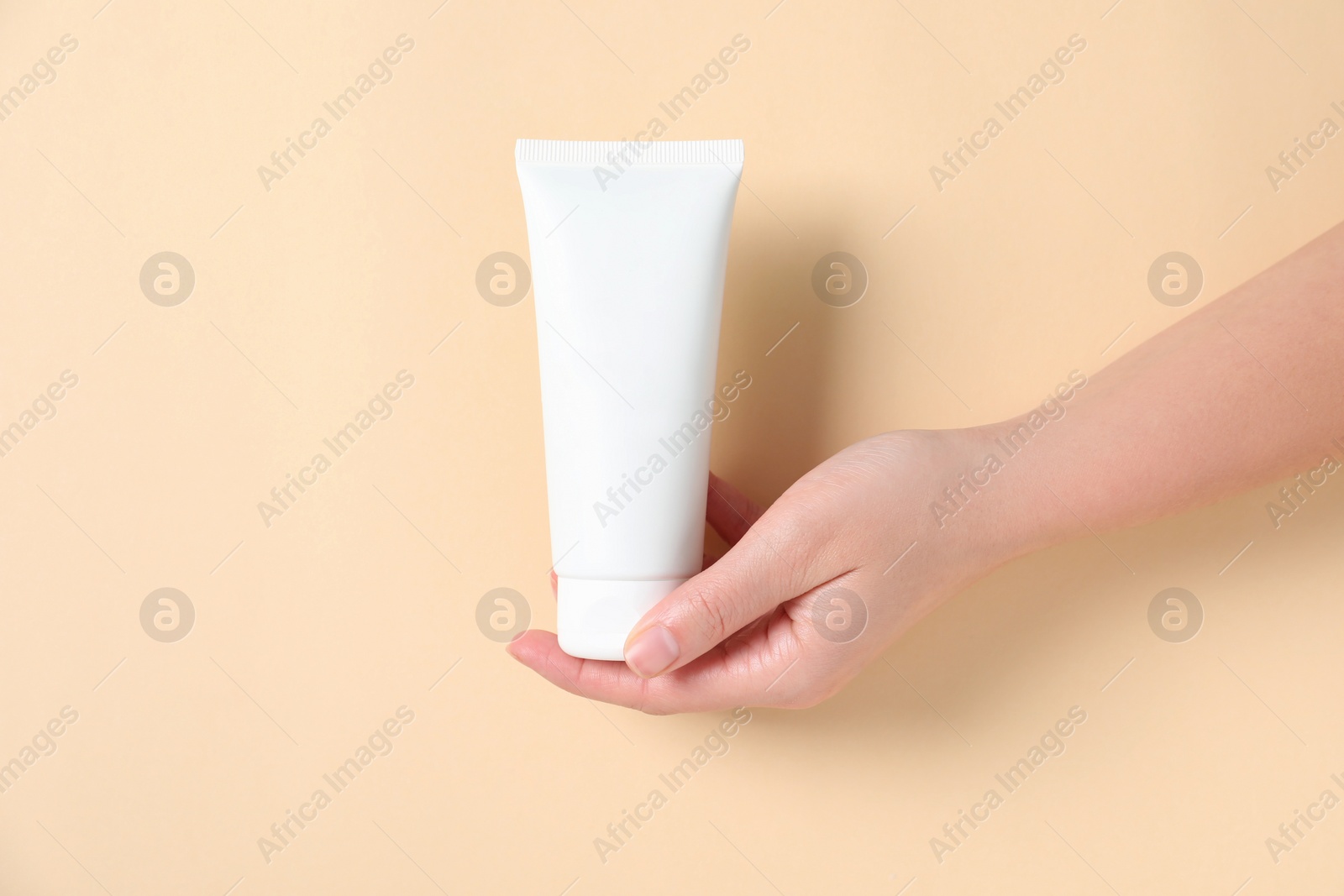 Photo of Woman with tube of hand cream on beige background, closeup