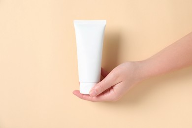 Woman with tube of hand cream on beige background, closeup