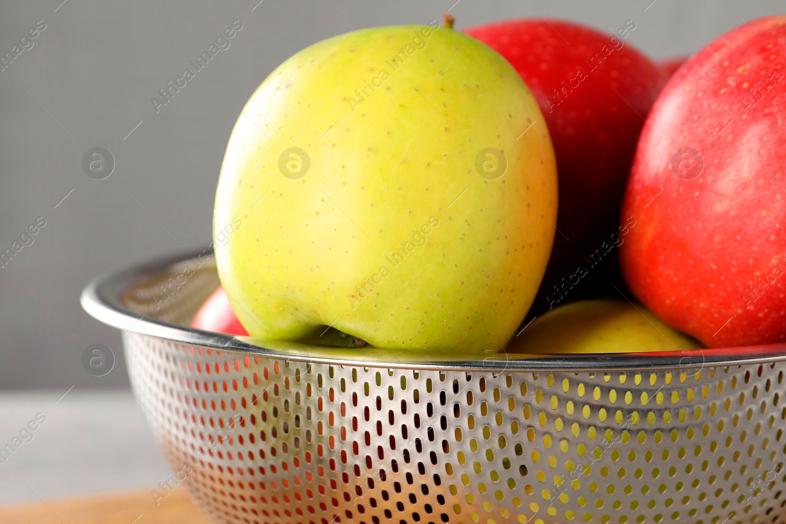 Photo of Fresh ripe apples in colander on light grey background, closeup