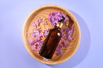 Bottle with essential oil, lilac flowers and water in bowl on violet background, top view