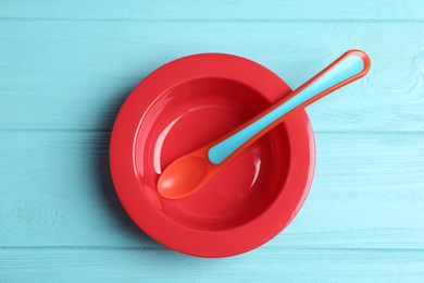 Plastic plate and spoon on light blue wooden table, top view. Serving baby food