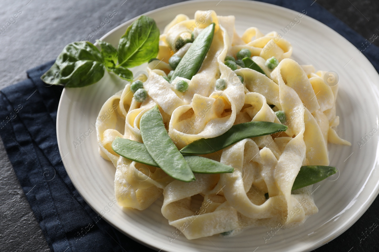 Photo of Delicious pasta with green peas and creamy sauce on black table, closeup