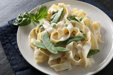 Delicious pasta with green peas and creamy sauce on black table, closeup