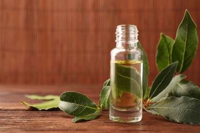 Bottle of bay essential oil and fresh leaves on wooden table. Space for text