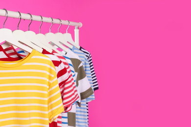 Photo of Colorful clothes hanging on rack against  pink background. Space for text