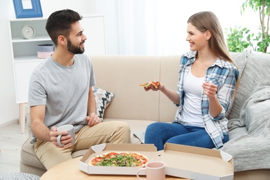 Young couple having pizza for lunch in living room. Food delivery