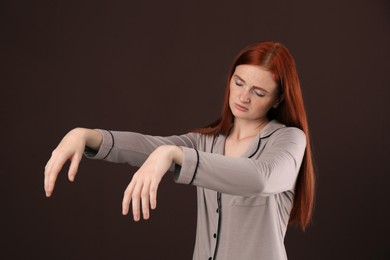 Photo of Young woman wearing pajamas in sleepwalking state on brown background