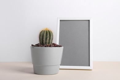 Beautiful cactus in pot and frame on beige table