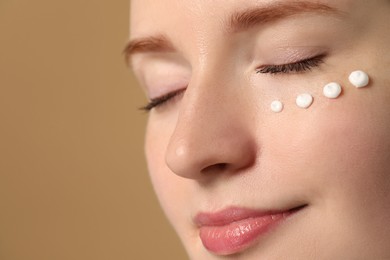 Photo of Beautiful woman with freckles and cream on her face against beige background, closeup. Space for text