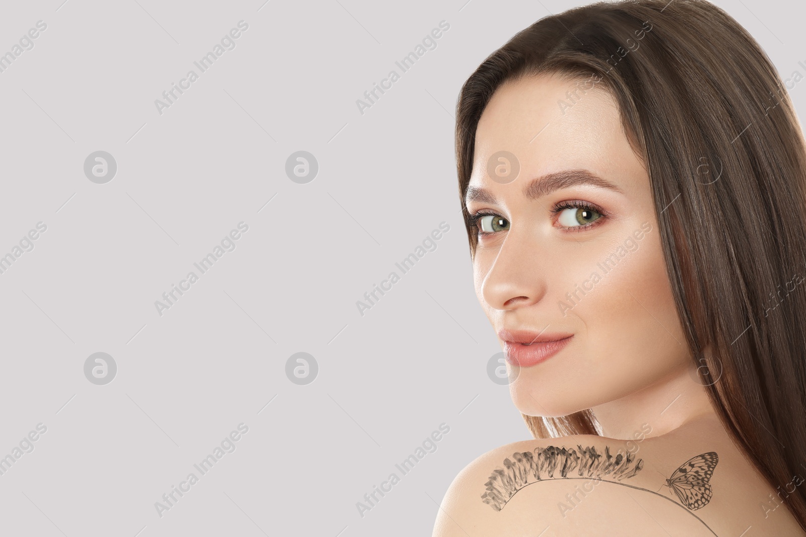 Image of Smiling young woman with tattoo of flower and butterfly on light background, space for text