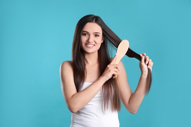 Beautiful smiling young woman with hair brush on color background