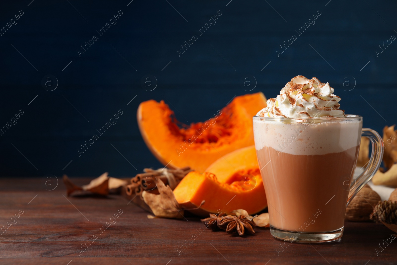 Photo of Delicious pumpkin latte and ingredients on brown wooden table. Space for text