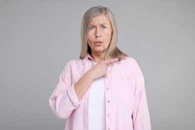Photo of Surprised senior woman pointing at something on grey background