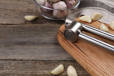 Garlic press and cloves on wooden table, closeup. Space for text
