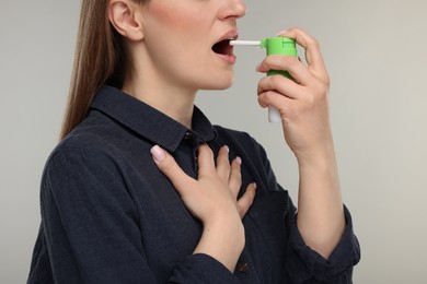 Woman using throat spray on grey background, closeup