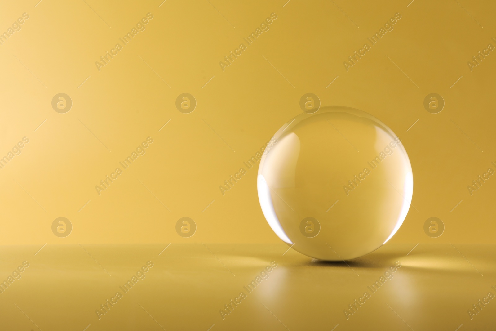Photo of Transparent glass ball on yellow background. Space for text