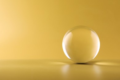 Photo of Transparent glass ball on yellow background. Space for text