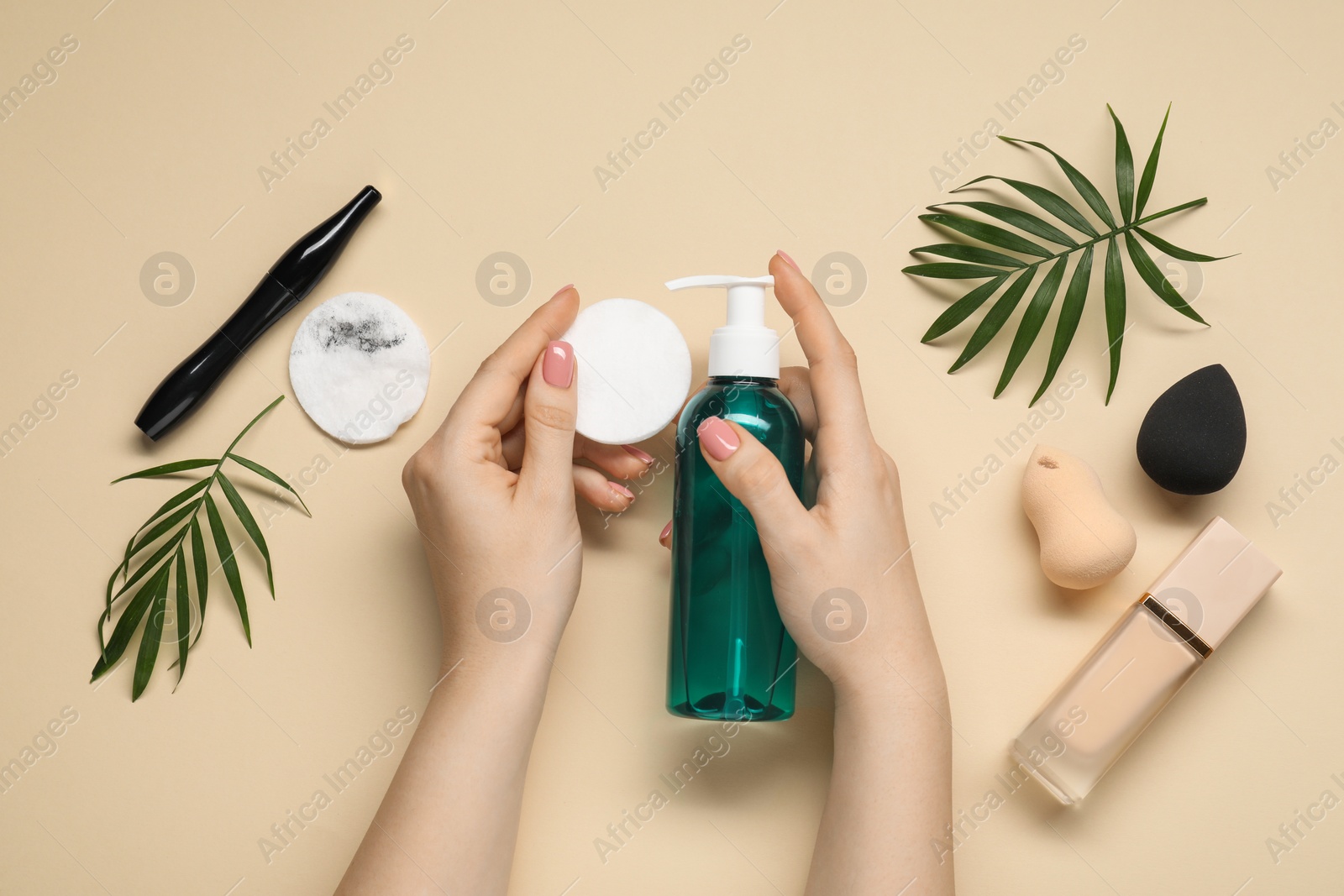 Photo of Woman with makeup remover, cotton pads, foundation, mascara and sponges on beige background, top view