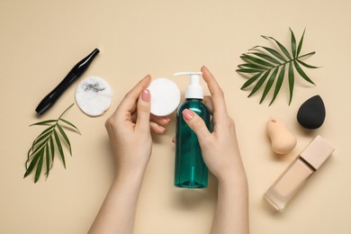 Photo of Woman with makeup remover, cotton pads, foundation, mascara and sponges on beige background, top view