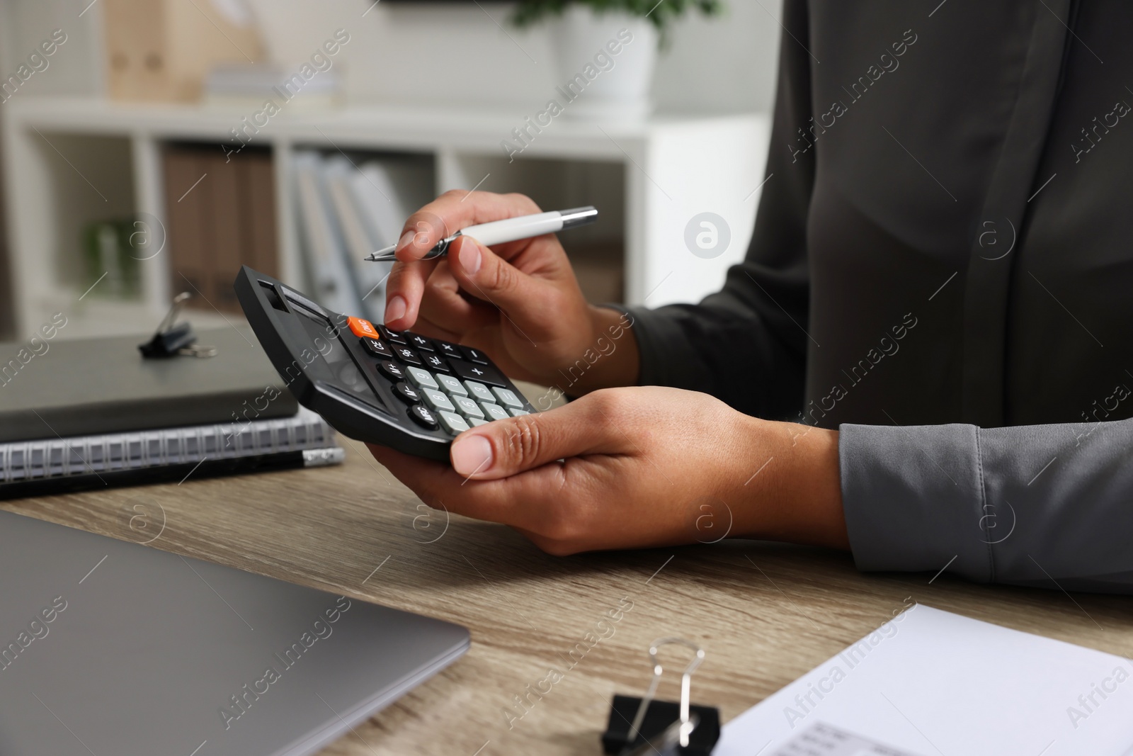 Photo of Woman using calculator at wooden table, closeup