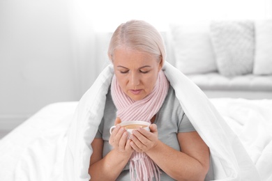 Photo of Ill mature woman with cup of hot tea for cough at home