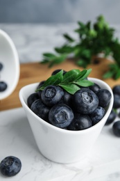 Photo of Bowl of tasty fresh blueberries and leaves on stone board, space for text