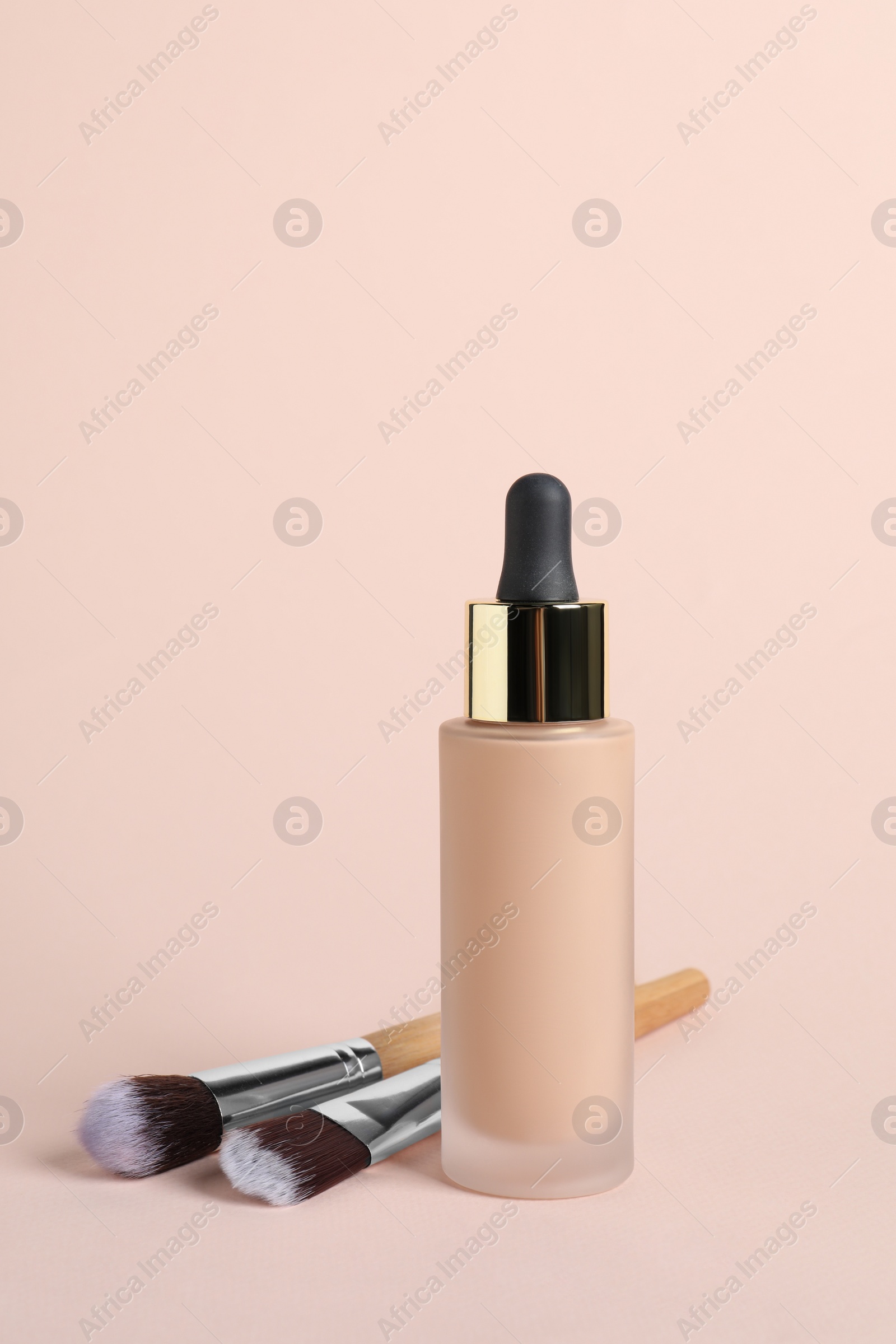 Photo of Bottle of skin foundation and brushes on beige background. Makeup product