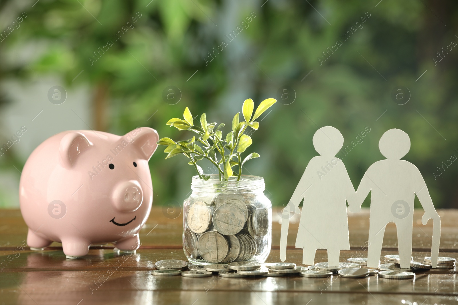 Photo of Pension savings. Figures of senior couple, jar with coins, piggy bank and green twigs on wooden table outdoors