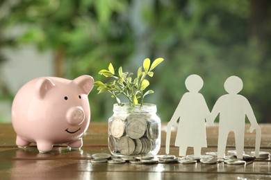 Pension savings. Figures of senior couple, jar with coins, piggy bank and green twigs on wooden table outdoors