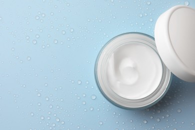 Photo of Jar of face cream on light blue surface covered with water drops, flat lay. Space for text