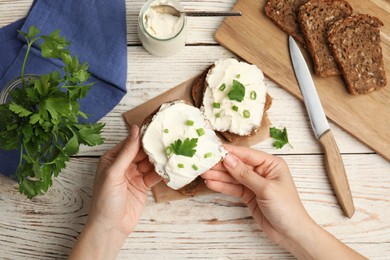 Photo of Woman holding bread with cream cheese at white wooden table, closeup