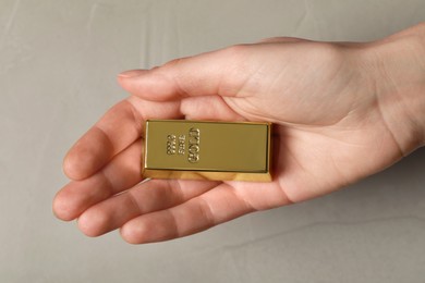 Woman holding gold bar against grey textured background, closeup