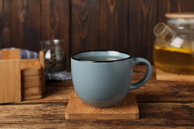 Photo of Mug of hot drink and stylish cup coaster on wooden table