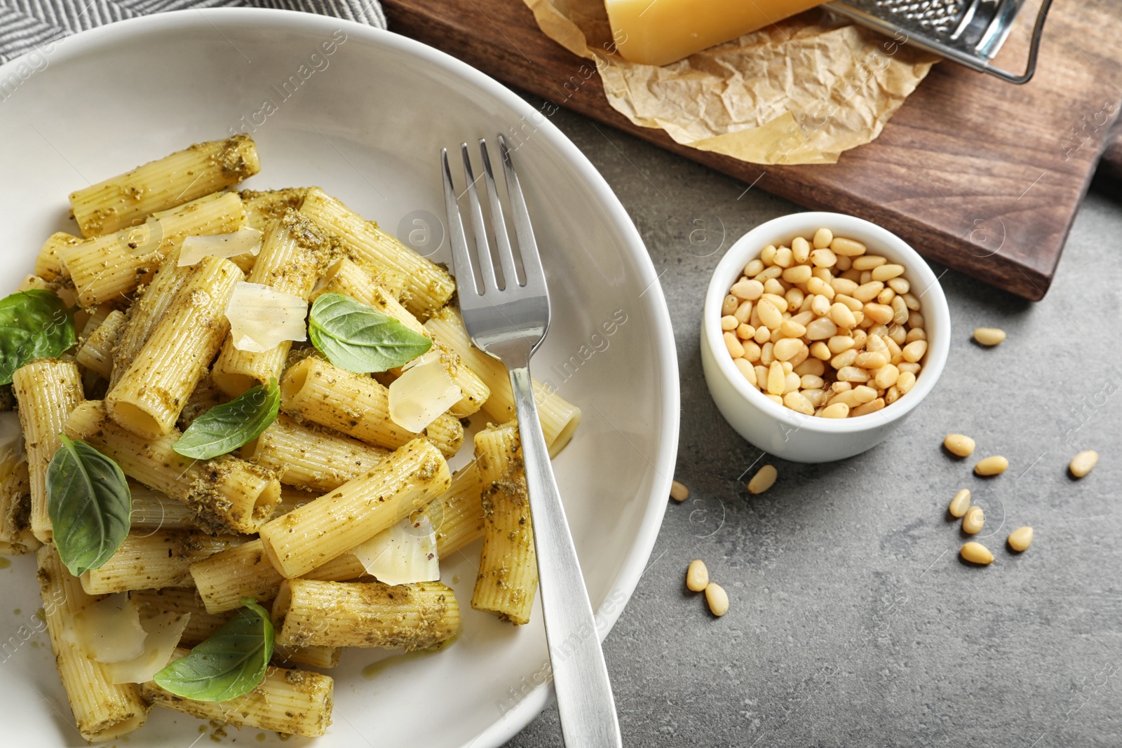 Photo of Flat lay composition with plate of delicious basil pesto pasta on gray table