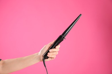 Photo of Woman holding clipless curling hair iron on pink background, closeup