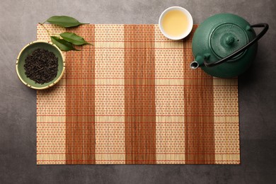 Photo of Flat lay composition with bamboo mat, teapot and cup of tea on grey table. Space for text