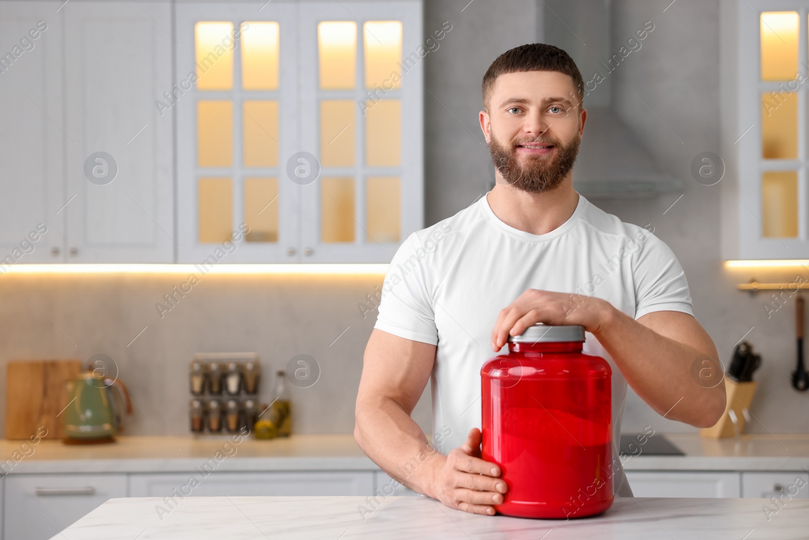 Photo of Young man with jar of protein powder at white marble table in kitchen, space for text