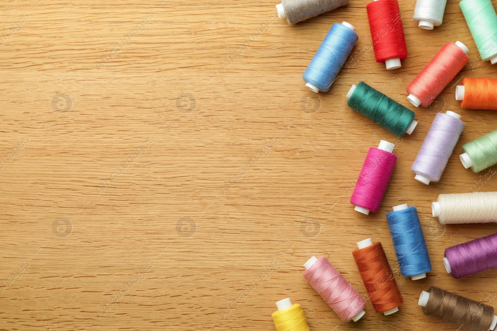 Photo of Many colorful sewing threads on wooden table, flat lay. Space for text