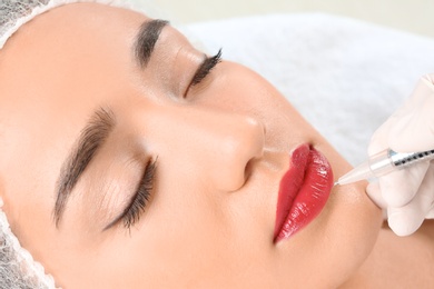 Young woman getting permanent makeup on lips in beautician salon, closeup