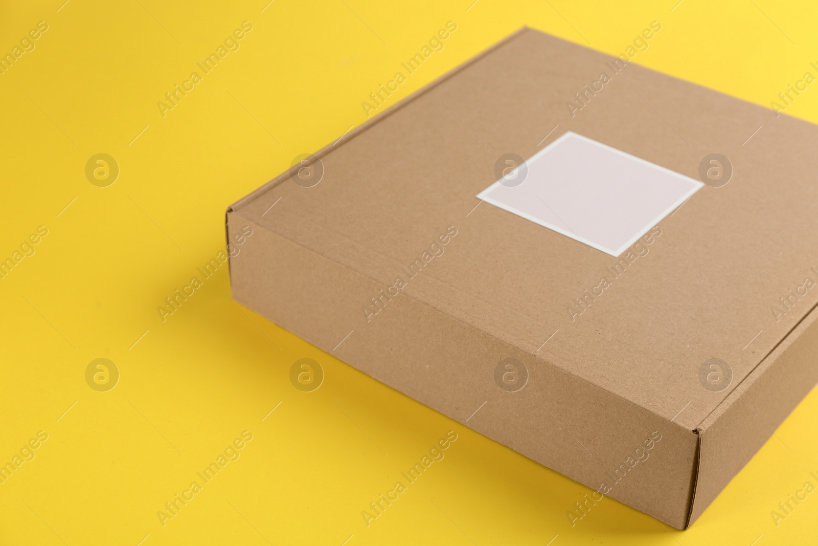 Photo of Closed cardboard box on yellow background, closeup