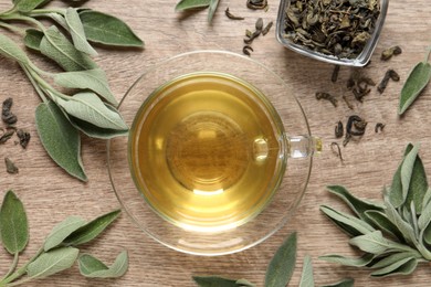 Photo of Cup of aromatic sage tea, dry and fresh leaves on wooden table, flat lay