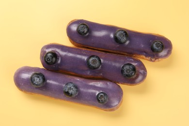 Photo of Delicious purple eclairs decorated with blueberries on yellow background, top view