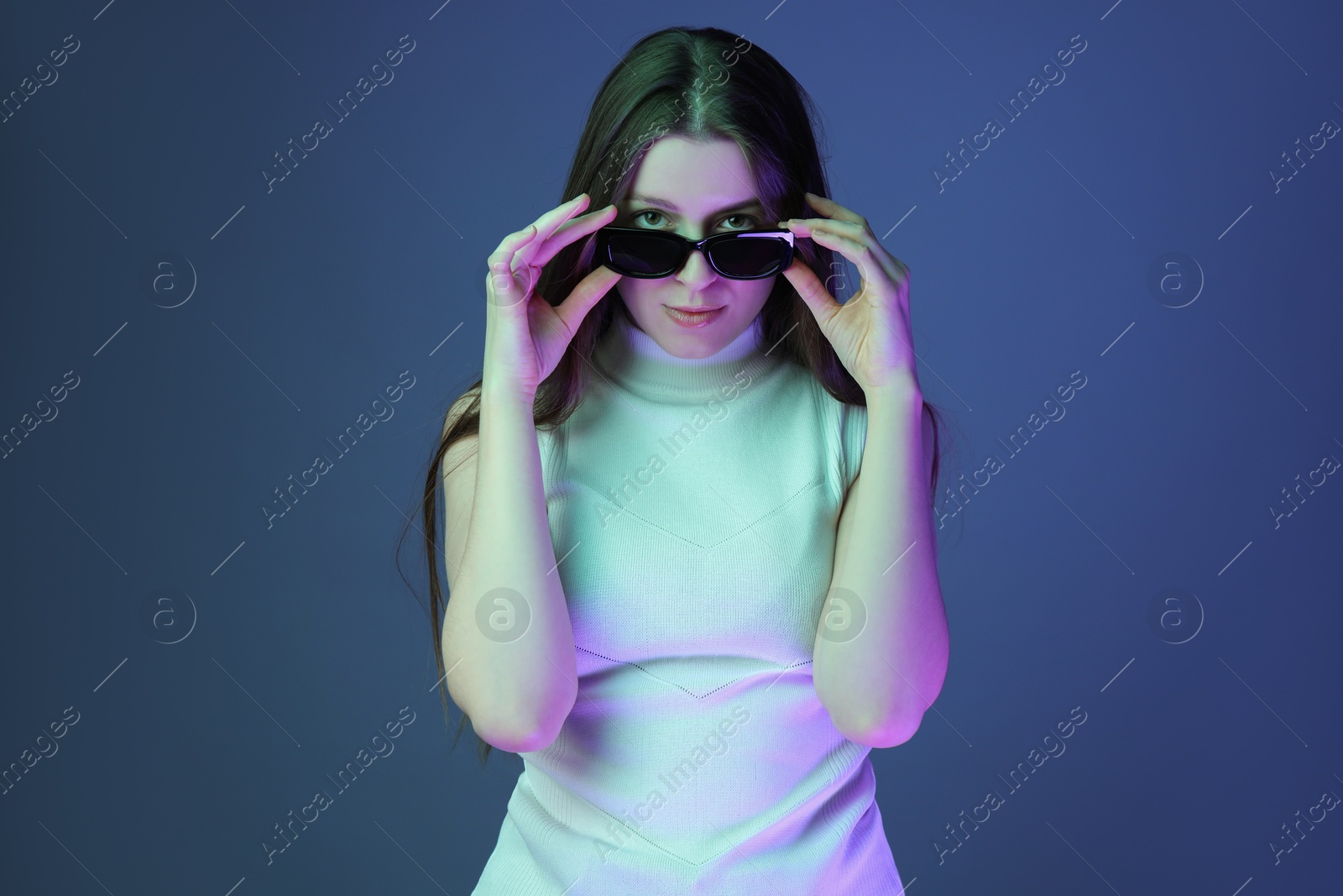 Photo of Portrait of beautiful young woman with sunglasses on color background with neon lights